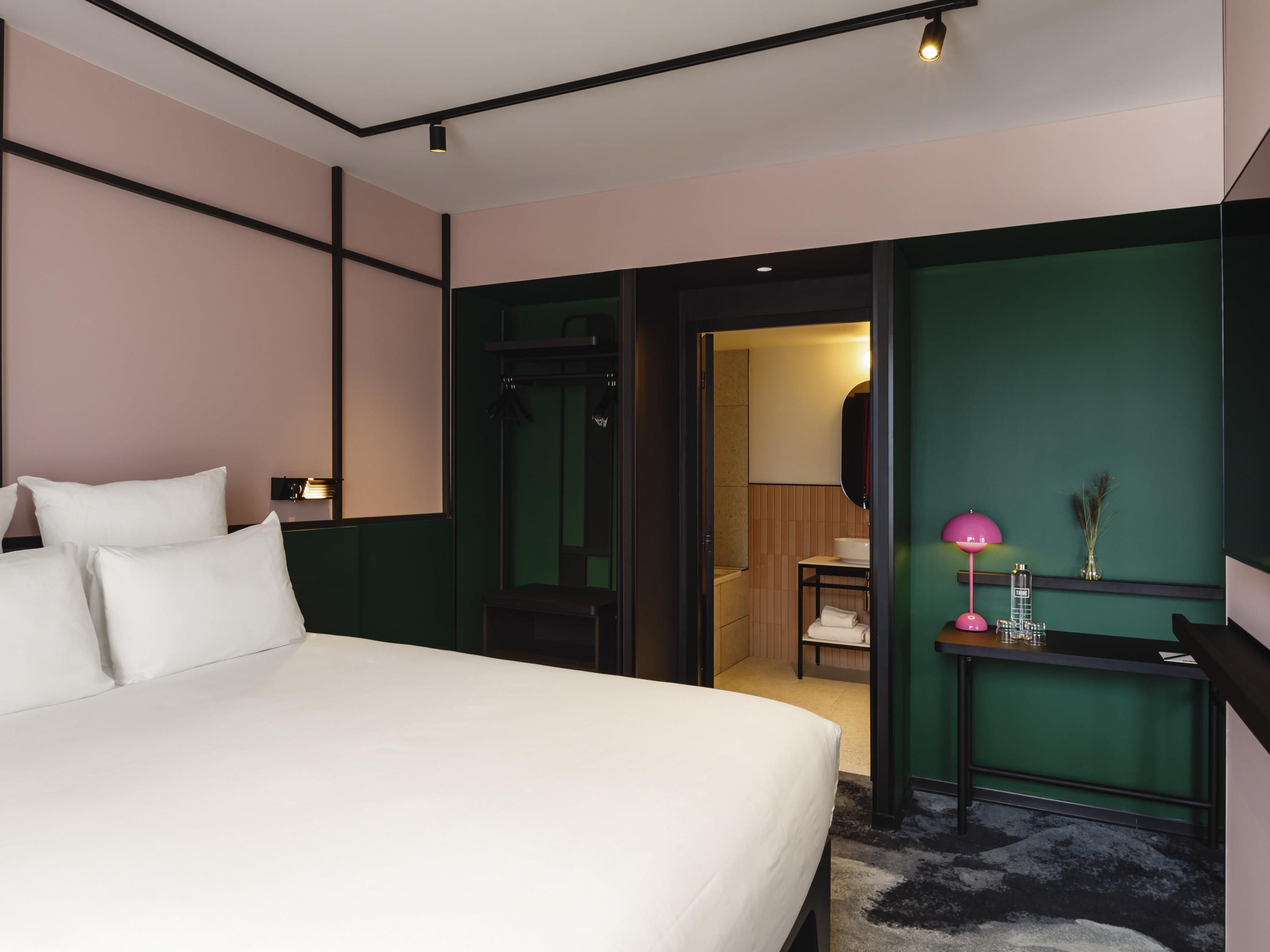 Habitación de hotel con cama, escritorio, silla y baño visible a través de una puerta abierta.