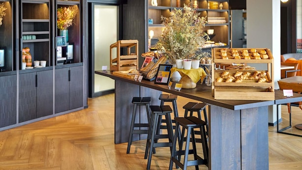 A modern café interior with a central bar area, wooden stools, and a variety of baked goods displayed on the counter.