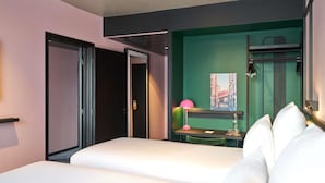 A modern hotel room with a bed, a desk, a chair, and a green accent wall.