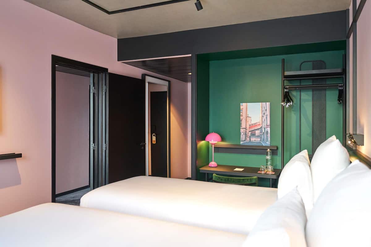 Una habitación de hotel moderna con cama, escritorio, silla y una pared de acento verde.