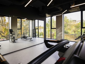 A gym with exercise equipment, large windows, and a view of trees.
