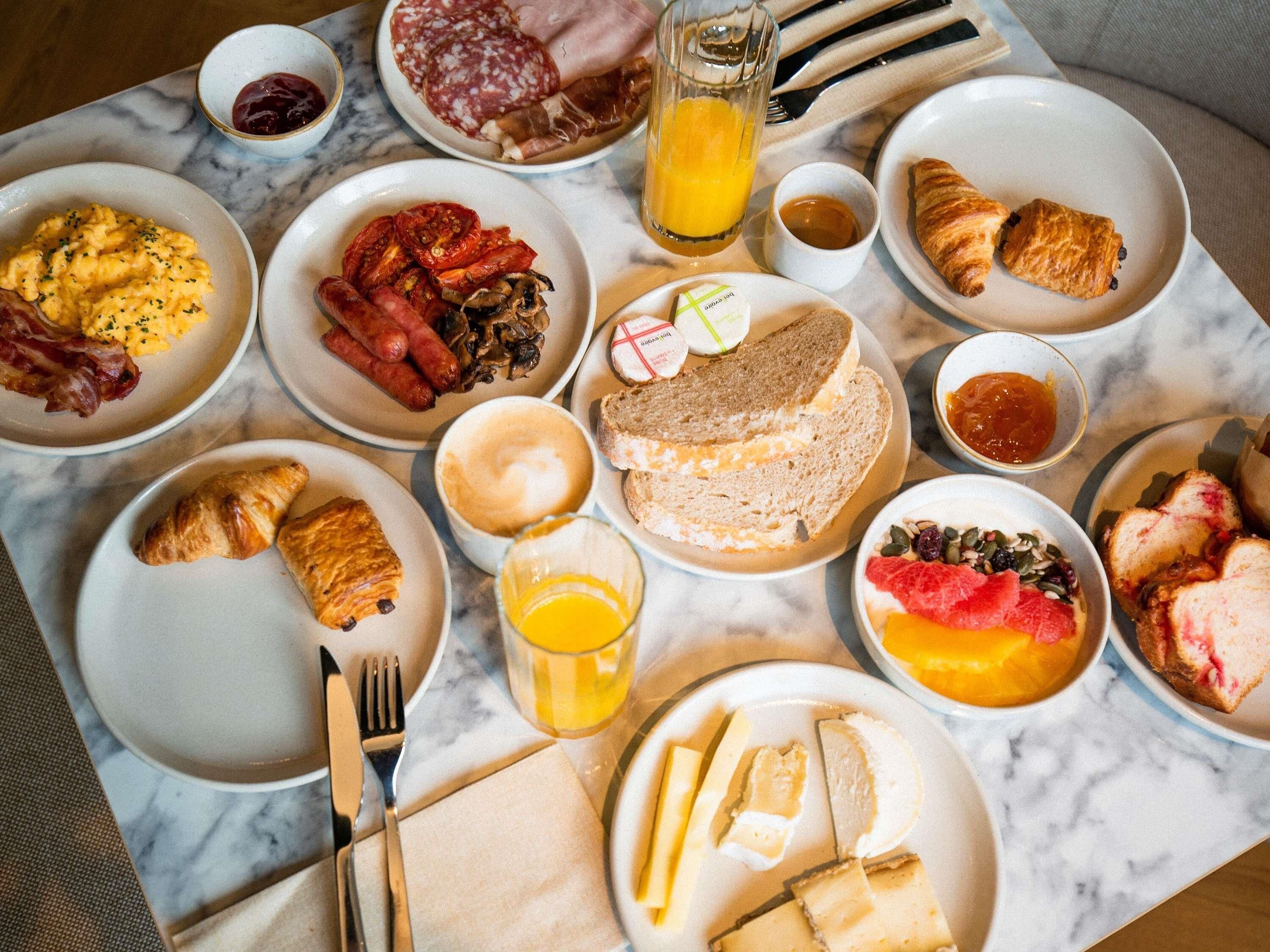 Ein reichhaltiges Frühstücksbuffet mit verschiedenen Speisen, darunter Eier, Wurst, Croissants und Käse.