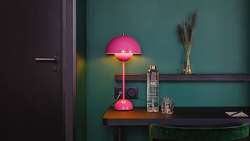 A room with a dark door, a teal wall, a pink desk lamp, a bottle labeled 'TRIBE', and a green chair.