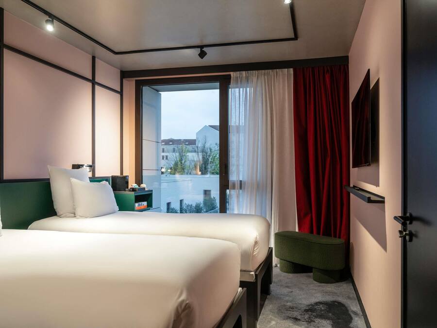 Una habitación de hotel moderna con una cama grande, un pequeño banco, un televisor y vistas al exterior.