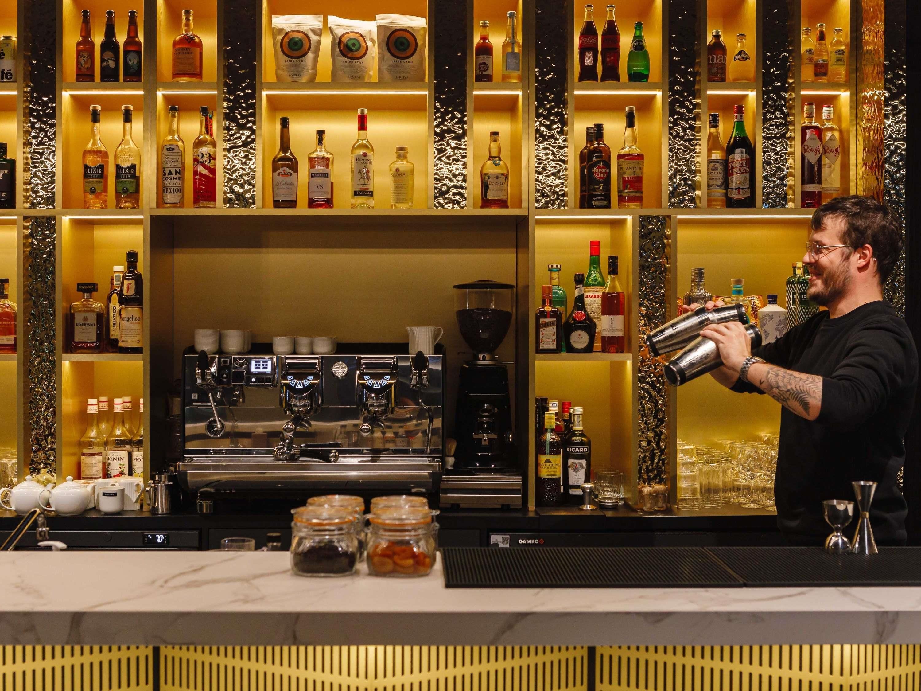 A bar area with shelves of liquor bottles, a coffee machine, and a bartender preparing drinks.