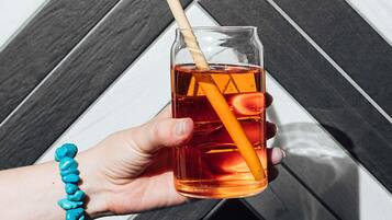 A hand holding a glass with a straw, containing a red beverage, against a geometric patterned background.