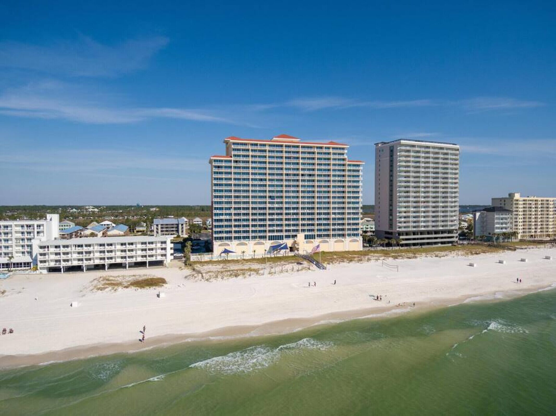Un hôtel situé en bord de mer, composé de plusieurs bâtiments, avec une plage de sable fin et un ciel bleu dégagé.