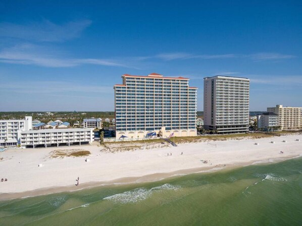 A beachfront hotel with multiple buildings, a sandy beach, and a clear blue sky.