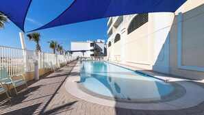 En swimmingpool med parasol, liggestole og en hvid bygning med altaner.