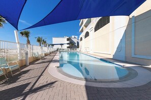 Una piscina con ombrellone, lettini e un edificio bianco con balconi.