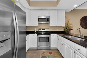 A modern kitchen with stainless steel appliances, white cabinetry, and a black countertop.