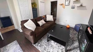 A living room with a brown sofa, a black coffee table, and a TV on a stand. - Lake-Themed Private Guest Suite Gated Community Pet Friendly Near I-4 (Plant City)