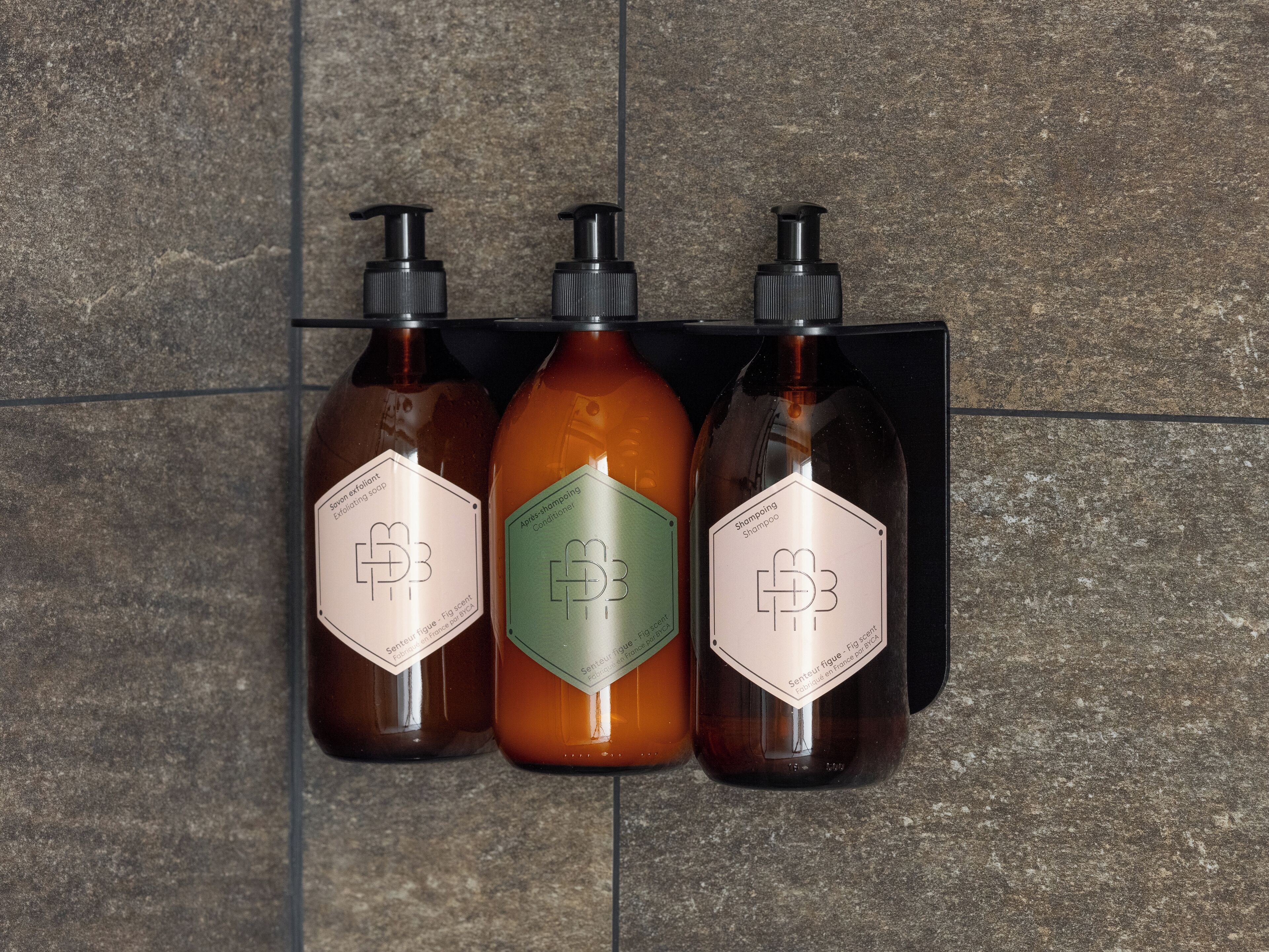 Three bottles of hair care products with pump dispensers mounted on a tiled wall.
