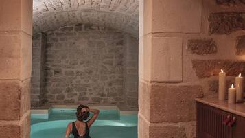 A stone-walled room with a bathtub, candles, and a wooden cabinet.