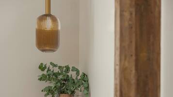 A corner of a room with a wooden table, a potted plant, a small stool, and a hanging light fixture.