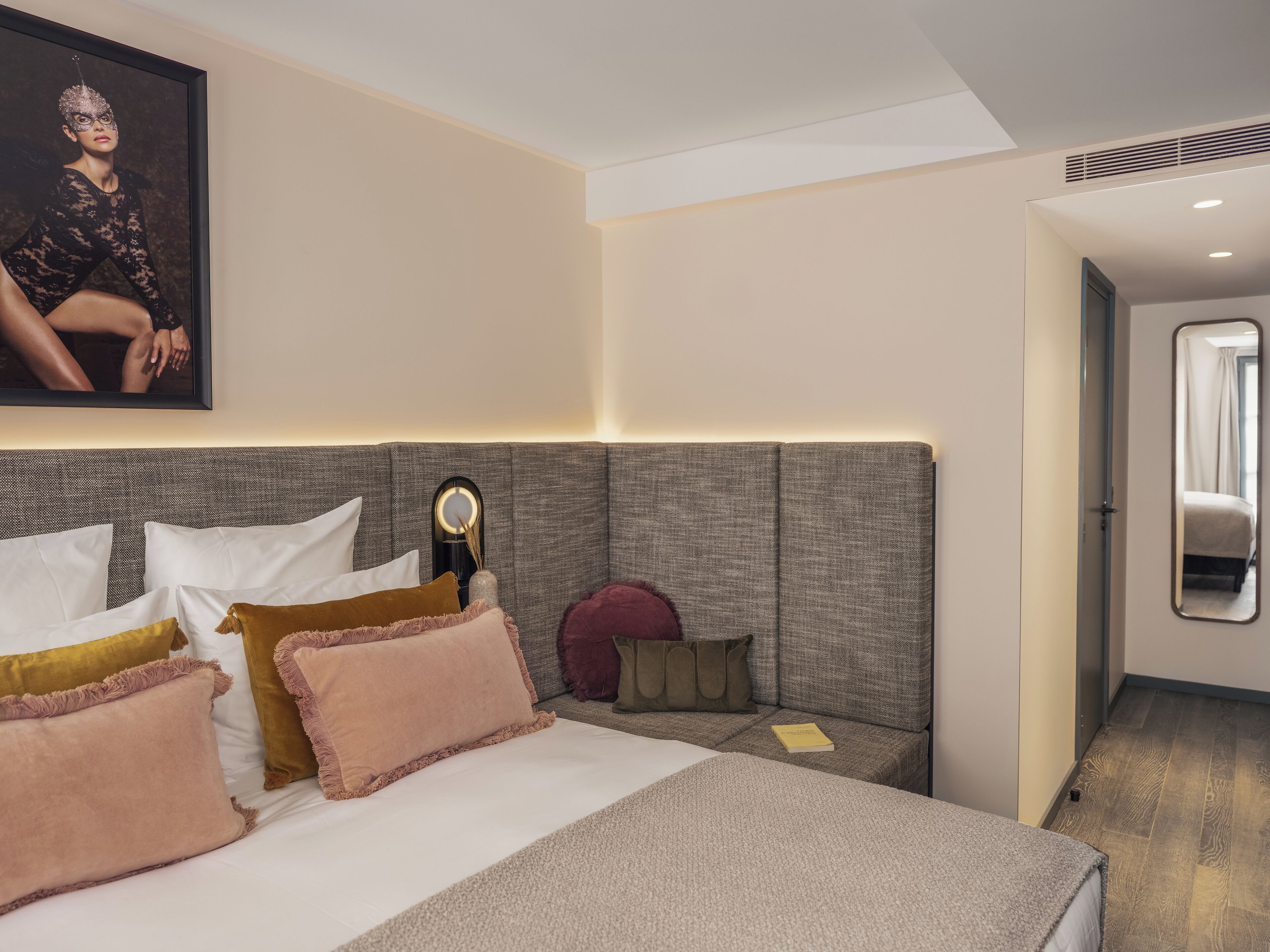 Una habitación de hotel moderna con una cama grande, una mesita de noche con lámpara y un cuadro enmarcado en la pared.
