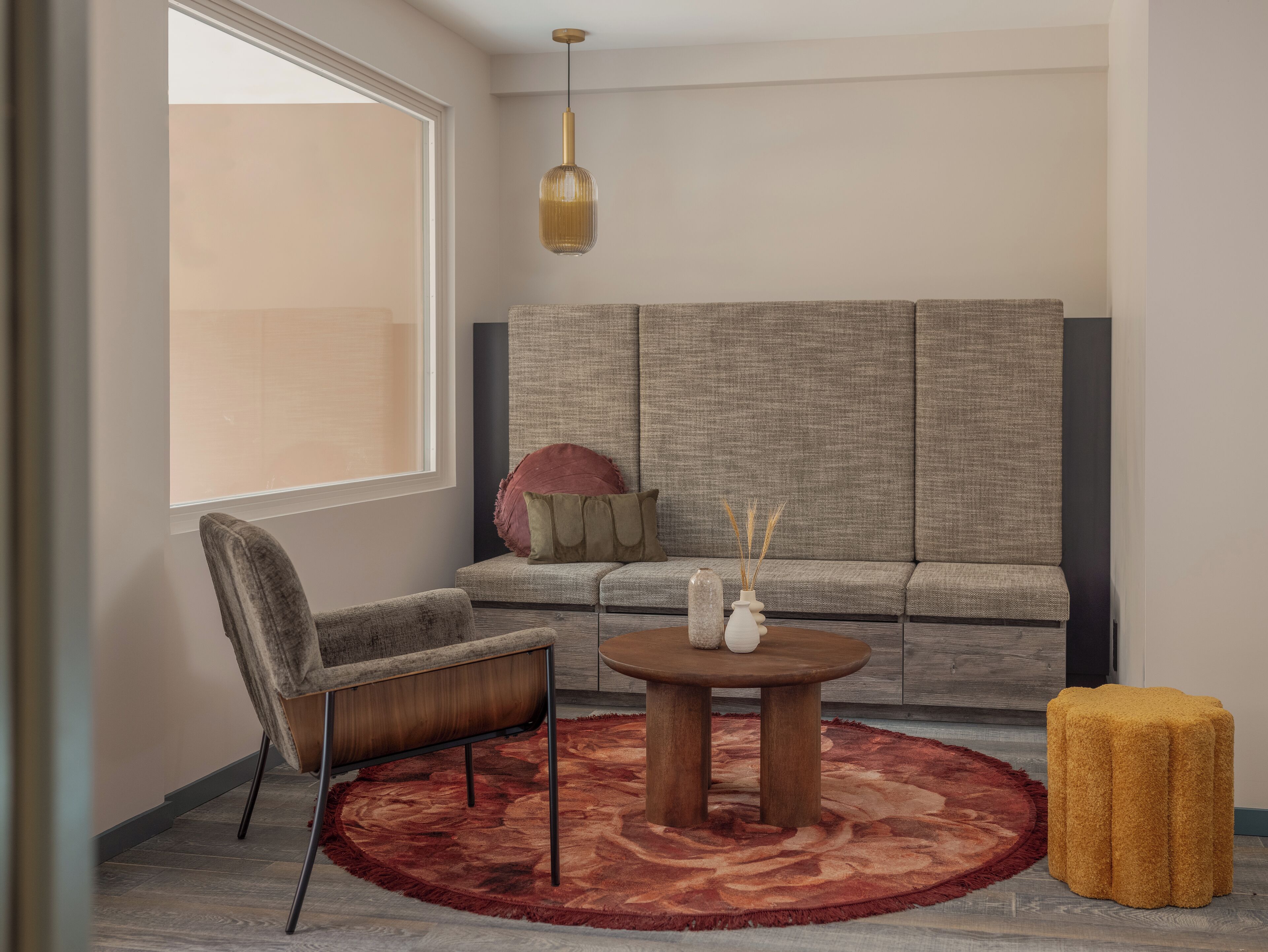 A modern living room with a sofa, a round coffee table, a chair, a yellow ottoman, and a hanging light fixture.