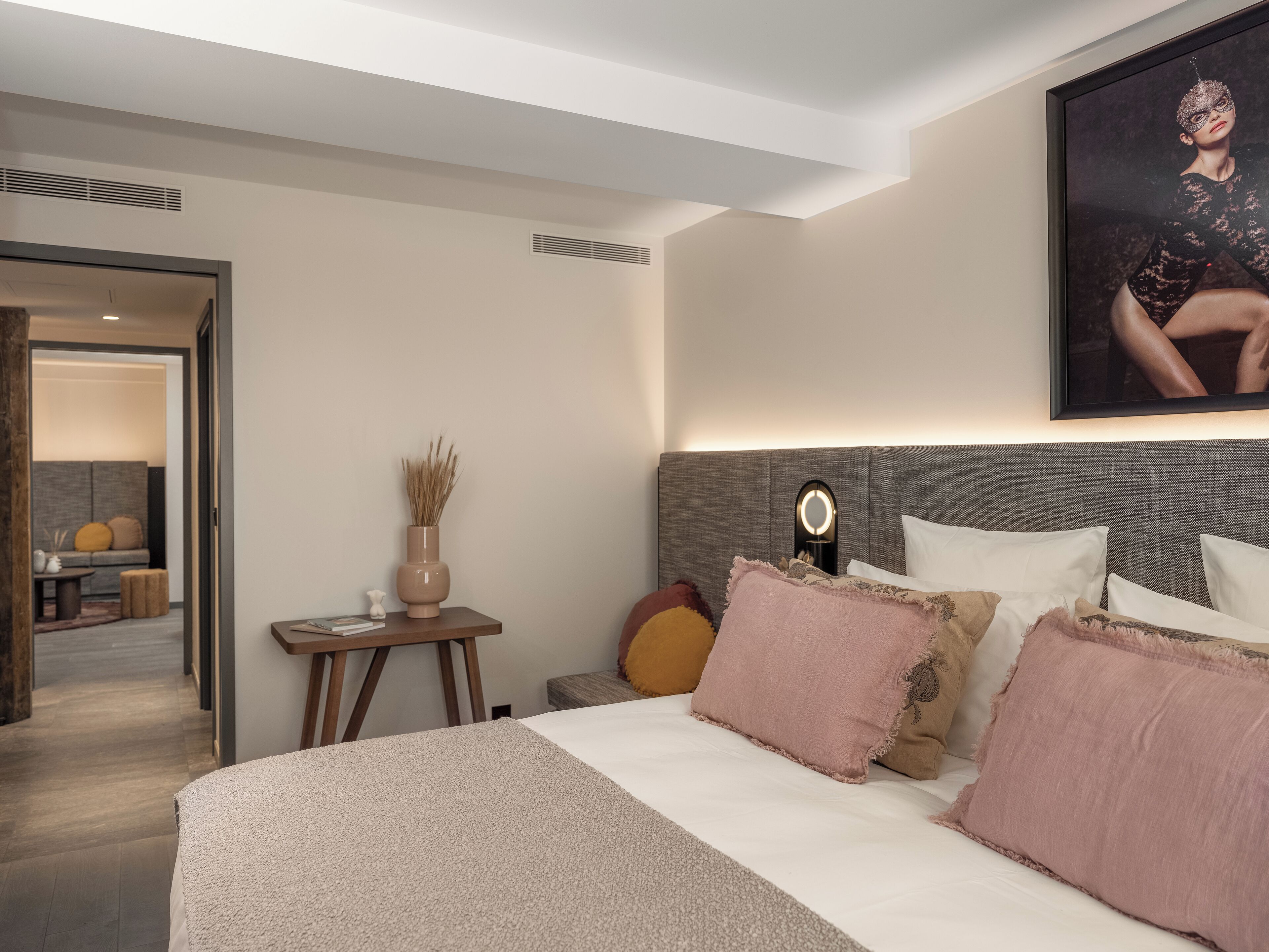 Een moderne hotelkamer met een groot bed, een nachtkastje met een vaas en een spiegel aan de muur.