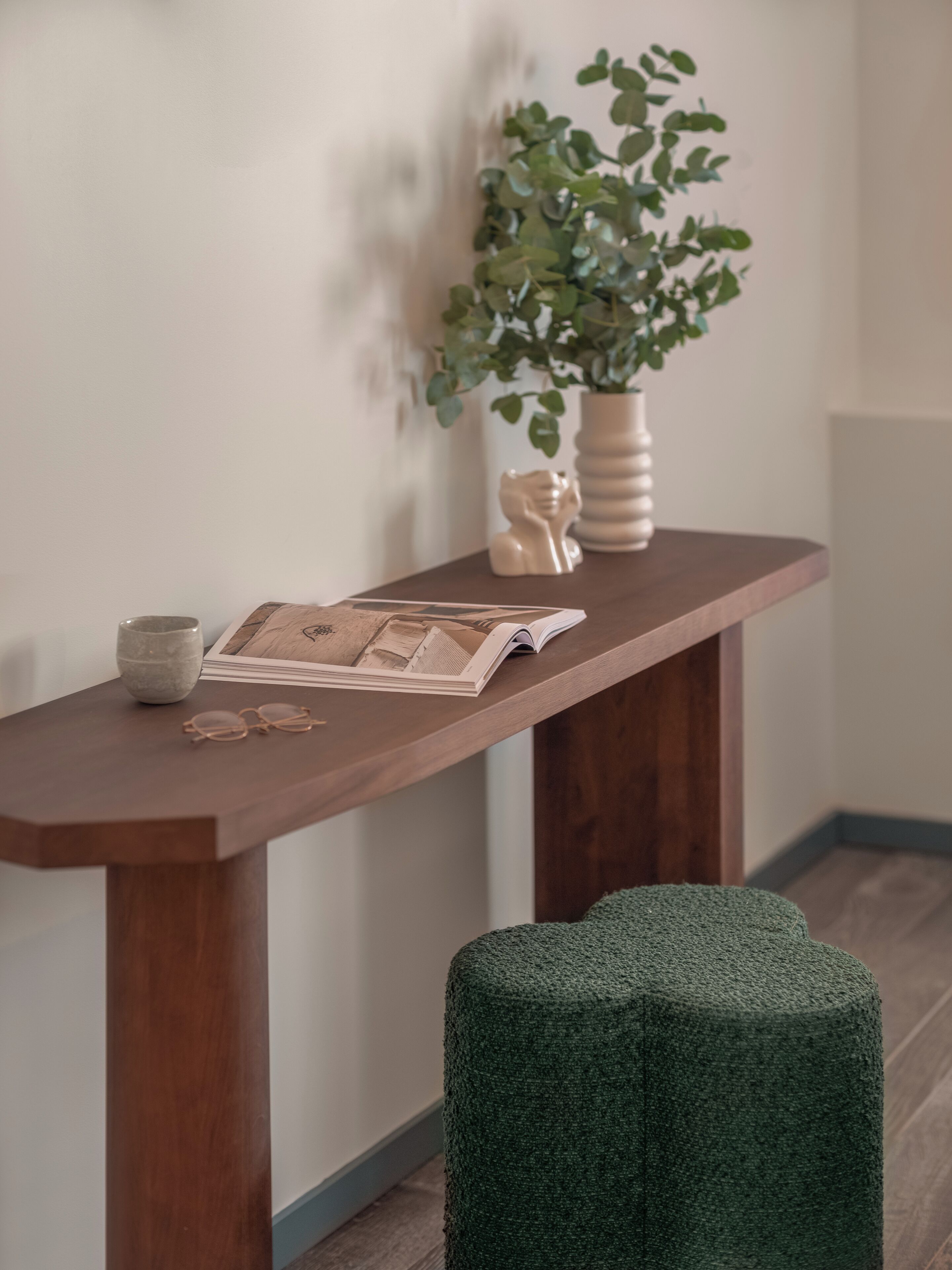 A wooden console table with a vase, a plant, a pair of glasses, and an open magazine.