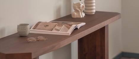 A wooden console table with a vase, a plant, a pair of glasses, and an open magazine.