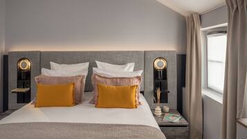 Una habitación de hotel moderna con una cama grande, dos mesitas de noche y un ventanal con cortinas.
