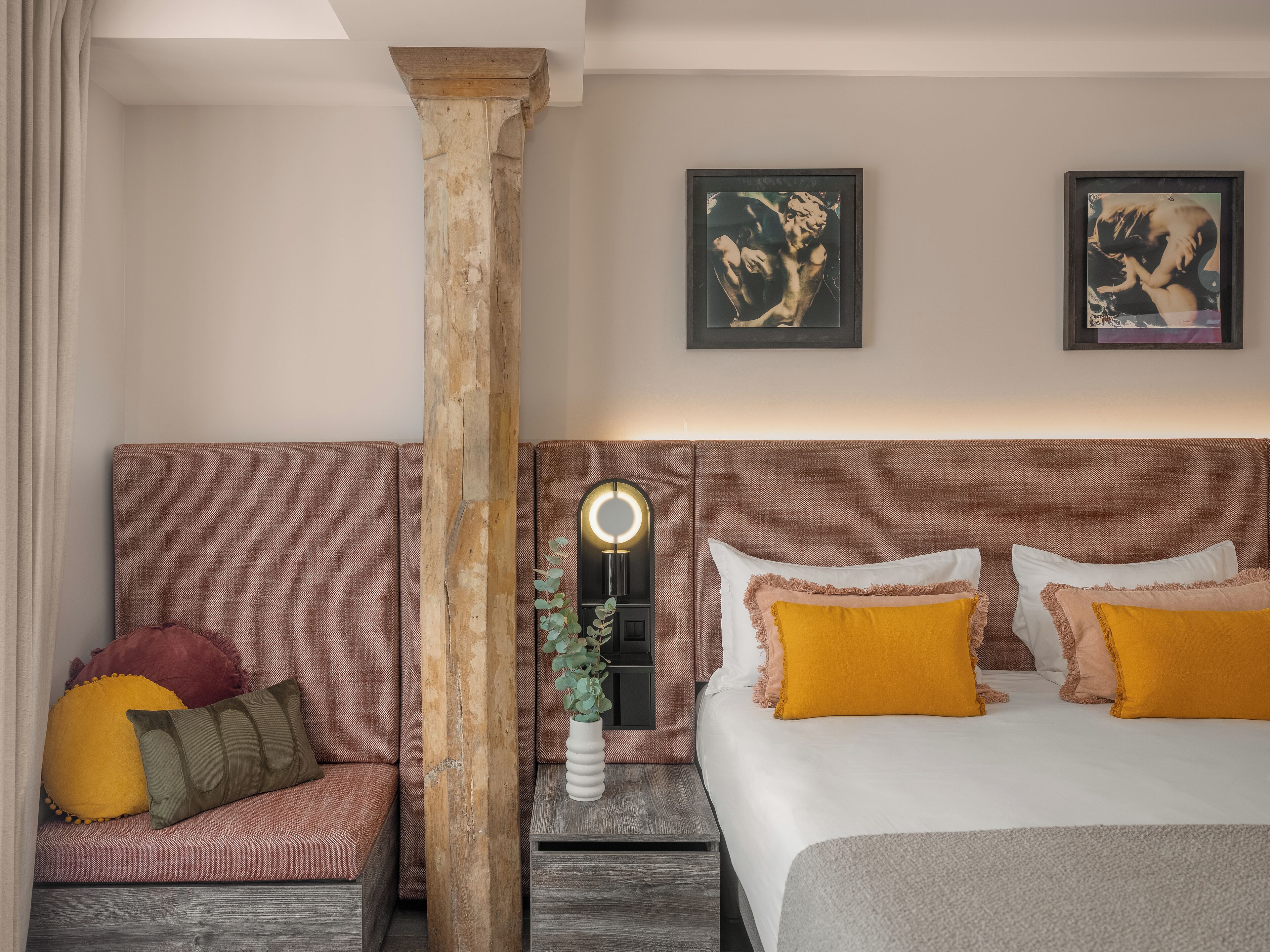 A hotel room with a large bed, a seating area with cushions, and two framed artworks on the wall.