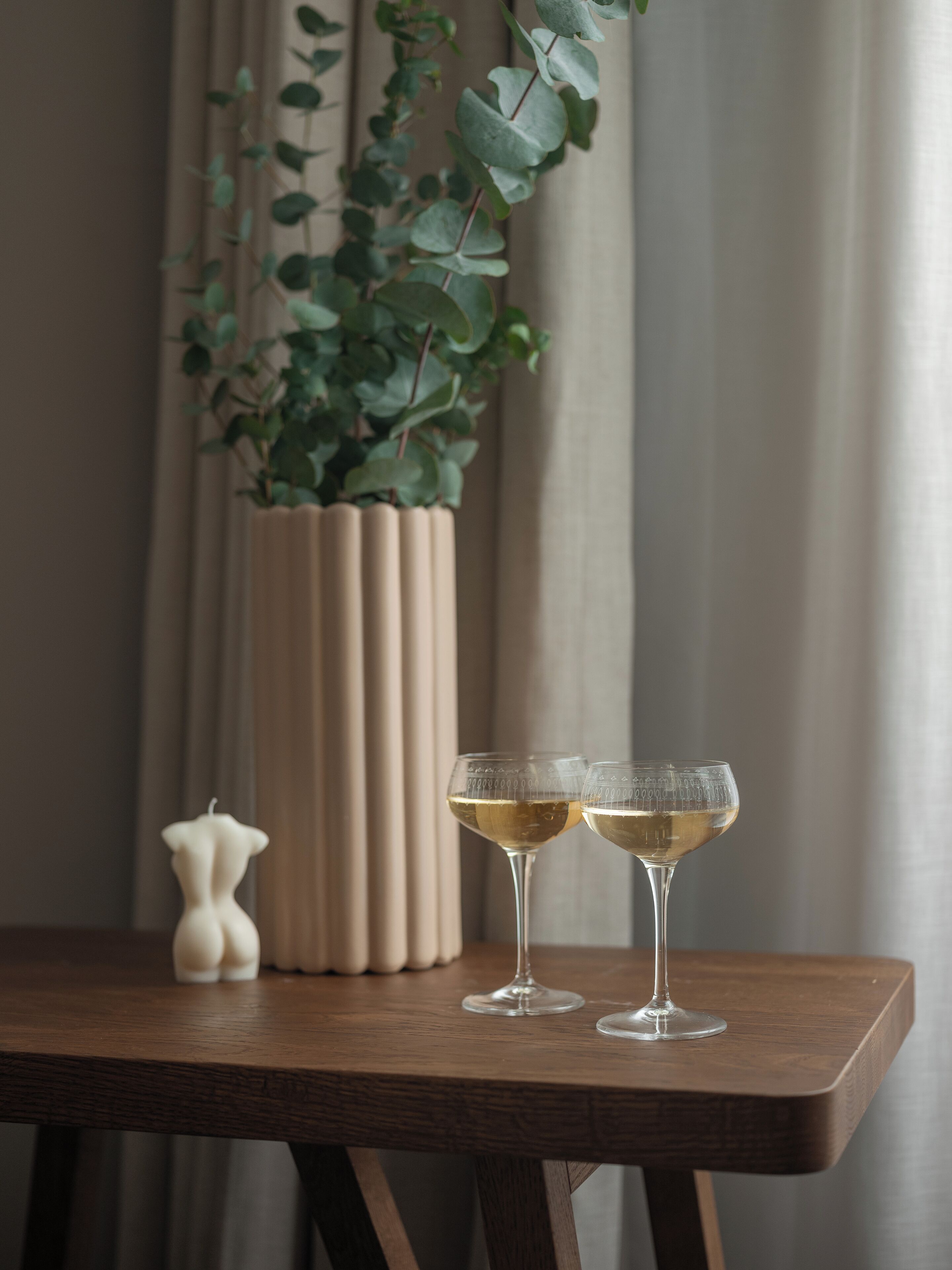 A table with two wine glasses and a vase of green leaves.