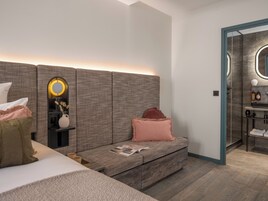 Un dormitorio moderno con una cama grande, una mesita de noche con espejo, un pequeño rincón de descanso y vistas al baño.