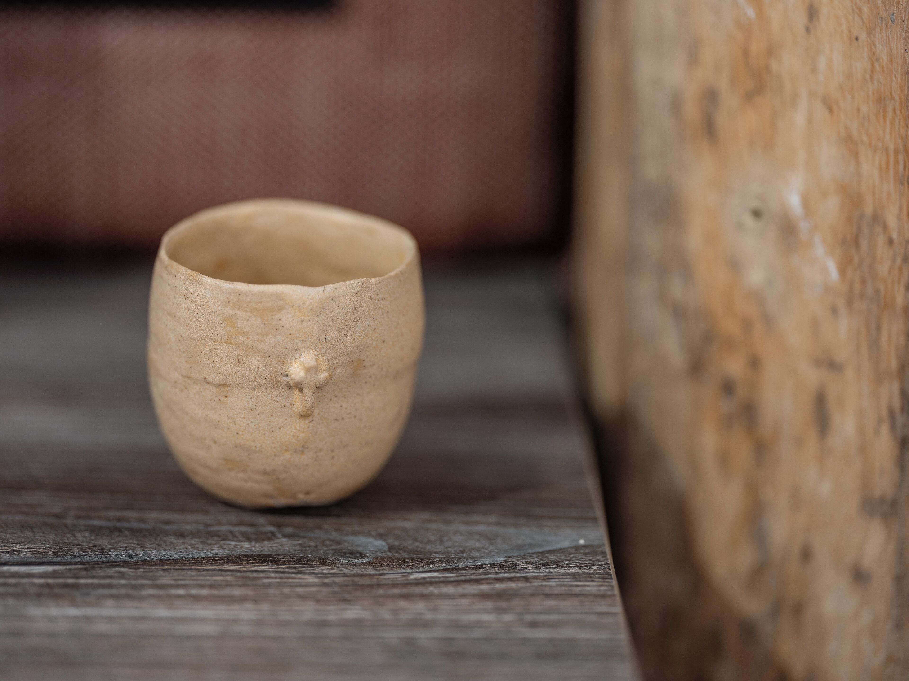 Una taza pequeña y sencilla de cerámica sobre una superficie de madera.