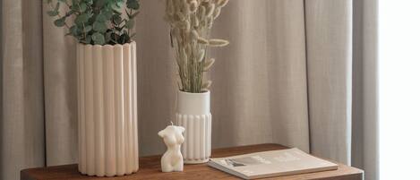A wooden table with two white vases, one with green foliage and the other with dried flowers, and a small white figurine.