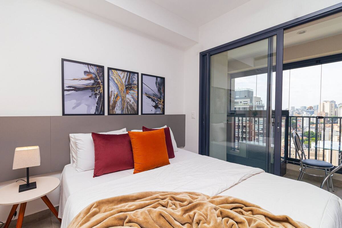 A modern hotel room with a large bed, a glass balcony, and abstract art on the wall.