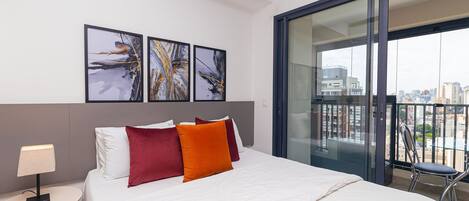 A modern hotel room with a large bed, a glass balcony, and abstract art on the wall.