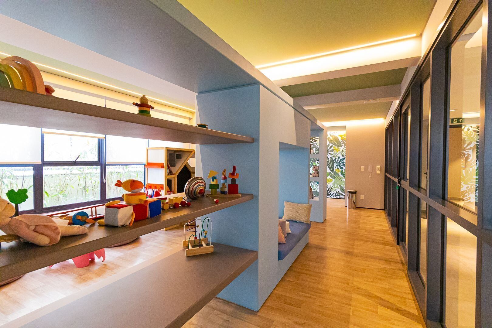 Un intérieur moderne avec un plancher en bois, un coin salon doté de coussins et des étagères où sont exposés divers objets.