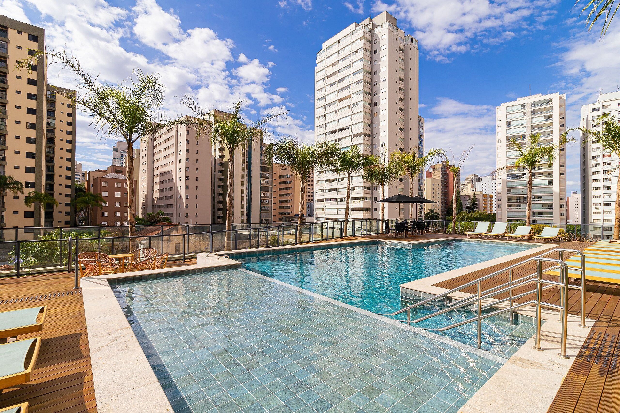 Une piscine avec une terrasse en bois, des chaises longues et de grands immeubles en arrière-plan.