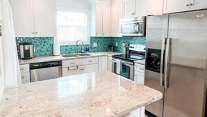 Una cocina moderna con armarios blancos, un refrigerador de acero inoxidable y una encimera de granito.