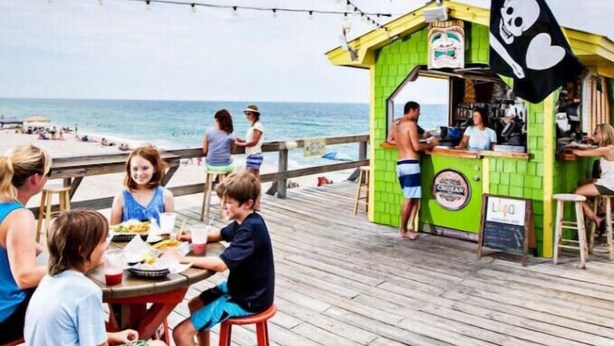 Un restaurante frente a la playa con terraza al aire libre y vistas al océano, con un letrero con temática pirata y fachada verde.