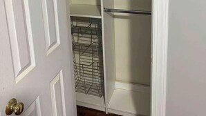 Un armario blanco con puertas abiertas, que muestra estantes y espacio para colgar.