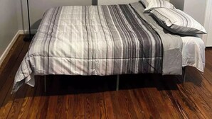 Un dormitorio con cama, lámpara de pie y suelo de madera.