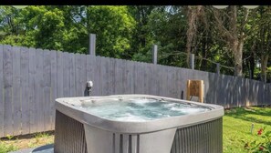 Un bain à remous dans un jardin, avec une clôture en bois et des arbres en arrière-plan.