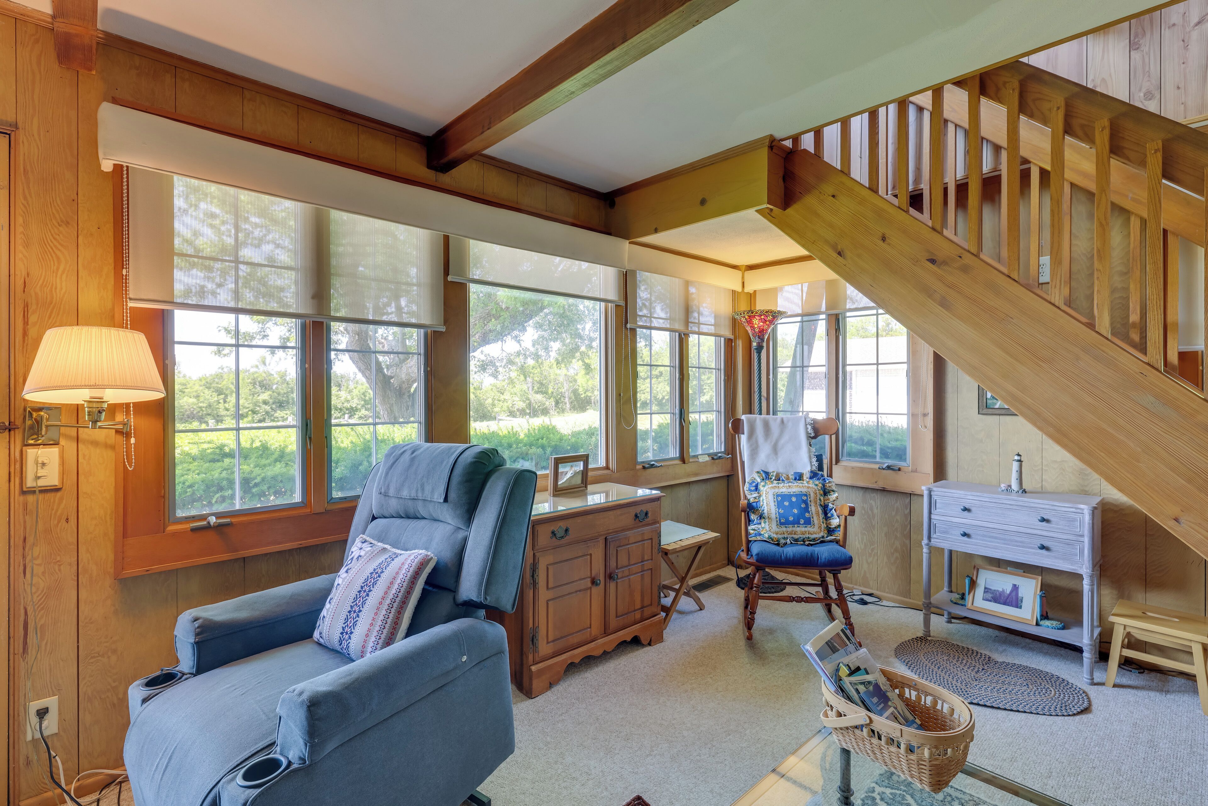 A cozy room with a wooden ceiling, large windows, a blue sofa, a wooden desk, and a chair.