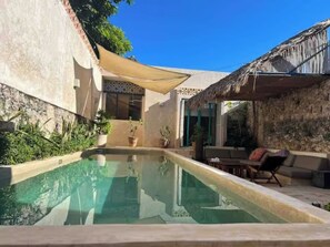 A swimming pool with a thatched roof structure, potted plants, and a clear blue sky. - Central & Bohemian House  Pool Yard (Mérida)
