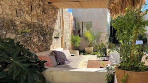 Un espace extérieur accueillant, avec un mur en pierre, un canapé confortable et divers pots de plantes.