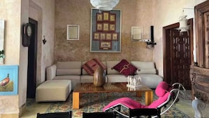 Un salon chaleureux avec un canapé, un pouf et une table basse, agrémenté d’un vase décoratif et d’une œuvre d’art murale.