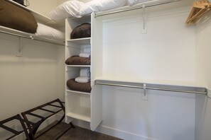 Un vestidor amplio con múltiples estantes y espacio para colgar, que incluye una barra metálica y un perchero de madera.