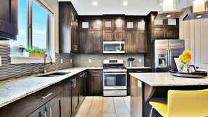 A modern kitchen with dark wood cabinets, stainless steel appliances, a granite countertop, and a yellow chair. - Entrada at Moab 420 and 424 and 428 (Moab)