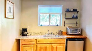 A compact kitchen with wooden cabinets, a built-in dishwasher, a toaster oven, and a window above the sink. - Central & Peaceful Getaway at Cozy Studio Apt.  (Toquerville)