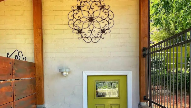 A green door with a decorative metal wall art above it, a metal gate to the right, and a wooden ceiling. - Central & Peaceful Getaway at Cozy Studio Apt.  (Toquerville)