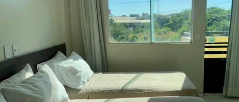 Habitación de hotel con dos camas, un ventanal con vistas a zonas verdes y edificios, y una puerta que da a un espacio exterior.