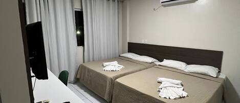 Een hotelkamer met twee bedden, een bureau met computer en telefoon, een televisie en een airconditioner.
