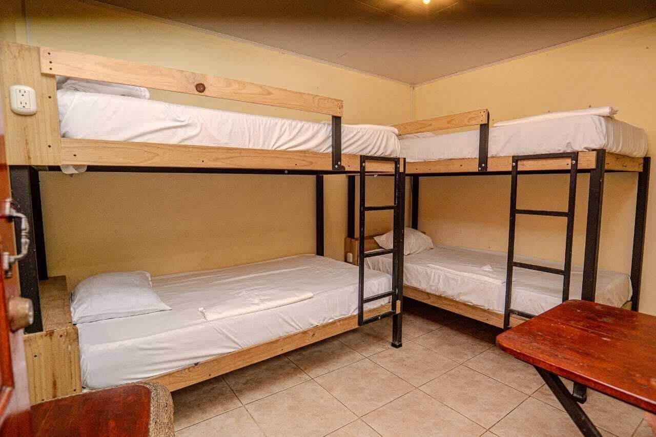 Ein Schlafraum mit Etagenbetten, einem Holztisch und einer Stehleiter.